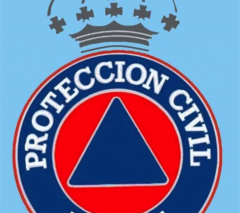 Escudo oficial de Protección Civil de España con un triángulo azul en el centro de un círculo rojo, rodeado por un anillo azul con el texto “Protección Civil España” y coronado por una corona real